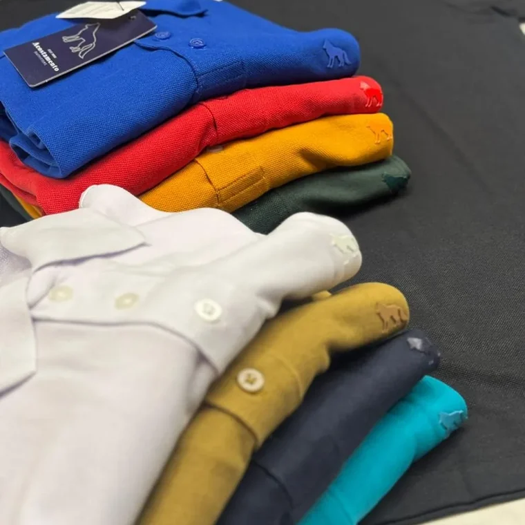 Pilha de camisas gola polo em piquê nas cores branco, mostarda, azul, vermelho e verde